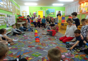 Dzieci siedzą na dywanie. Część dzieci przechodzi po kulach sensorycznych.
